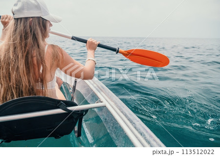 Woman in kayak back view. Happy young woman with long hair floating in transparent kayak on the crystal clear sea. Summer holiday vacation and cheerful female people relaxing having fun on the boat Woman in kayak back view. Happy young woman with long hair floating in transparent kayak on the crystal clear sea. Summer holiday vacation and cheerful female people relaxing having fun on the boat 113512022