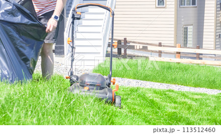 At a residential suburban house, a lush green lawn is meticulously mowed using an electric lawn mower, creating a well-manicured and inviting outdoor space. At a residential suburban house, a lush green lawn is meticulously mowed using an electric lawn mower, creating a well-manicured and inviting outdoor space. 113512460