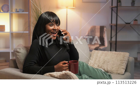 Phone talk. Excited woman. Home leisure. Happy female enjoying mobile communication drinking coffee in cozy living room interior. 113513226