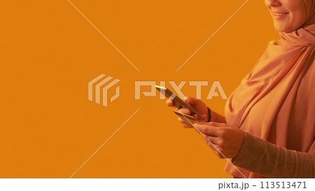 Online shopping. Mobile banking. Unrecognizable happy woman buying purchase with credit card on phone app internet payment on orange empty space background. Online shopping. Mobile banking. Unrecognizable happy woman buying purchase with credit card on phone app internet payment on orange empty space background. 113513471