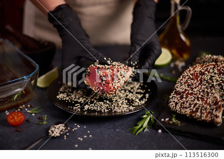 chef covers piece of tuna fillet with sesame seeds before cooking chef covers piece of tuna fillet with sesame seeds before cooking 113516300