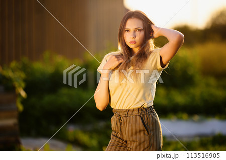 Photo shoot in countryside during golden hour, young European woman posing for photographer outdoors. 113516905
