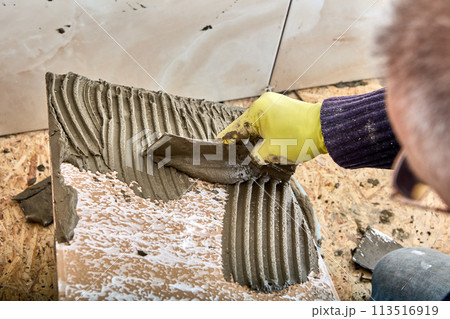 Using notched trowel to apply cement mortar tile adhesive to tiles. Using notched trowel to apply cement mortar tile adhesive to tiles. 113516919