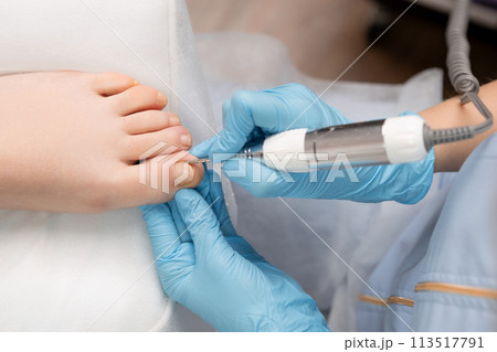 Pedicure master in rubber gloves making hardware pedicure using nail drill for woman. 113517791