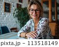 A woman wearing glasses sits at a table, engaged in an activity in a casual environment. 113518149