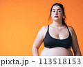 An expectant mother proudly shows off her baby bump in a black bikini while posing on the orange background 113518153