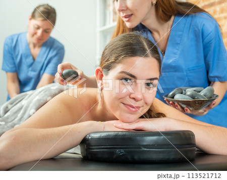 Smiling girl getting professional stone massage from two masseuse 113521712