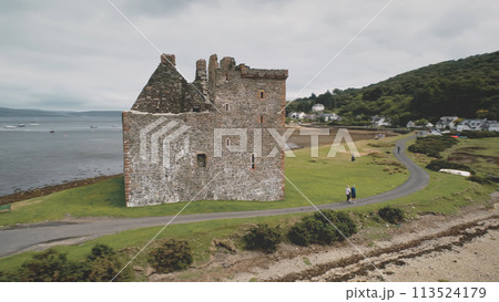 Closeup castle ruins at green mountain aerial. People walk on way of Loch Ranza ocean bay Closeup castle ruins at green mountain aerial. People walk on way of Loch Ranza ocean bay 113524179