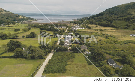Slow motion of Scottish whisky distillery at village aerial. Road, cottages, houses at green valley Slow motion of Scottish whisky distillery at village aerial. Road, cottages, houses at green valley 113524205