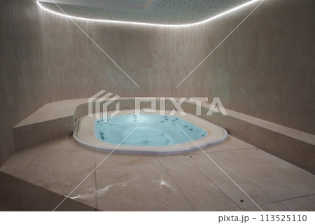 Luxurious indoor jacuzzi with beige marble tiles and bubbling water, creating a relaxing and elegant ambiance. Curved ceiling with soft lighting adds to the tranquil atmosphere. 113525110
