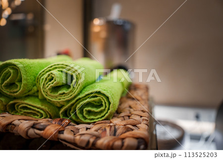 Close up view of lime green towels in a wicker basket, evoking comfort and cleanliness in a spa, gym, or bathroom setting. Accented by warm lighting, creating a tranquil atmosphere. Close up view of lime green towels in a wicker basket, evoking comfort and cleanliness in a spa, gym, or bathroom setting. Accented by warm lighting, creating a tranquil atmosphere. 113525203