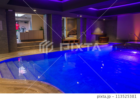 Luxurious indoor pool in a Zermatt hotel. Glowing blue water, modern architecture, whirlpool, reception desk. Tranquil and exclusive ambiance. Ideal for guests unwinding post skiing. Luxurious indoor pool in a Zermatt hotel. Glowing blue water, modern architecture, whirlpool, reception desk. Tranquil and exclusive ambiance. Ideal for guests unwinding post skiing. 113525381