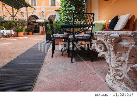 Luxury hotel outdoor seating area in Rome with terracotta flooring, pastel walls, elegant chairs, lush greenery, and tranquil ambiance for relaxation. Luxury hotel outdoor seating area in Rome with terracotta flooring, pastel walls, elegant chairs, lush greenery, and tranquil ambiance for relaxation. 113525517