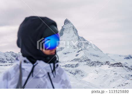 Person in white jacket, ski goggles, near Matterhorn mountain in Zermatt, Switzerland. Winter sports, alpine views, luxury accommodations in scenic photo. 113525880