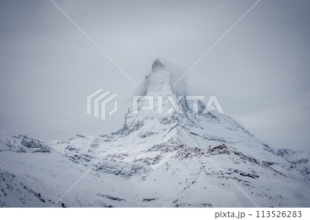This image captures the Matterhorn's serene grandeur in the Swiss Alps by Zermatt, showing its iconic peak in clouds above snow covered slopes, suggesting alpine activities in a winter wonderland. 113526283
