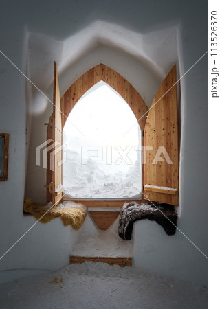 Interior of a snow covered room in Zermatt ski resort. Walls and floor made of snow, wooden door open to snow landscape. Cozy, rustic atmosphere with fur blankets. Interior of a snow covered room in Zermatt ski resort. Walls and floor made of snow, wooden door open to snow landscape. Cozy, rustic atmosphere with fur blankets. 113526370