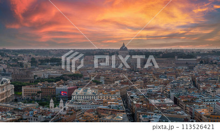 An aerial view of Rome at dusk reveals a sky changing from pink to blue, with the city in golden light. Key buildings and streets showcase its rich history and architectural variety. 113526421