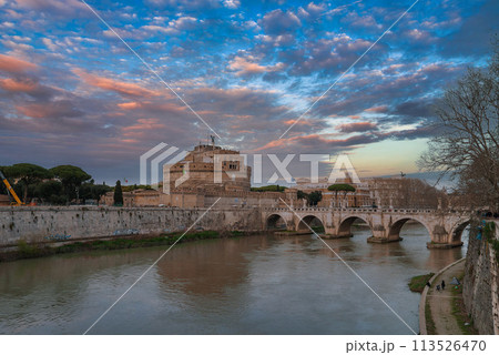 Scenic view of Castel Sant'Angelo in Rome, Italy. Overcast sky, Ponte Sant'Angelo bridge, historical fortress on Tiber River, trees, walkway, Italian flag. Scenic view of Castel Sant'Angelo in Rome, Italy. Overcast sky, Ponte Sant'Angelo bridge, historical fortress on Tiber River, trees, walkway, Italian flag. 113526470