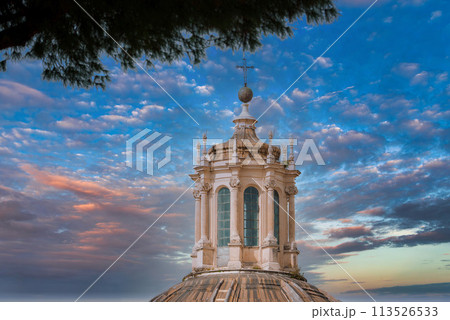 Baroque style dome with ornate lantern in European city. Ribbed design enhances aesthetic appeal under partly cloudy sky. Historical and religious architecture visible. 113526533