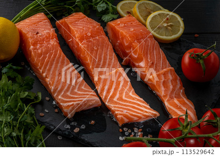 Fresh raw salmon fillet with cooking ingredients, herbs and lemon on black slate Fresh raw salmon fillet with cooking ingredients, herbs and lemon on black slate 113529642