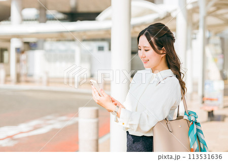 駅・ステーションのロータリーでスマホを使う女性(アプリ・モバイルチケット・チケットレス・電子乗車券) 駅・ステーションのロータリーでスマホを使う女性(アプリ・モバイルチケット・チケットレス・電子乗車券) 113531636
