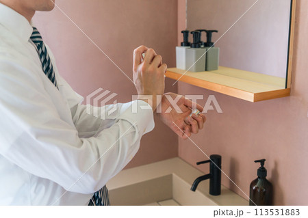 朝出勤前に手首に香水をつけるスーツ姿の若いアジア人ビジネスマン（メンズコロン・メンズ香水） 113531883