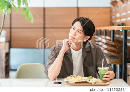 カフェでランチを食べながらグリーンスムージーを飲む若い男性（酵素・デトックス・食物繊維・健康食品） 113532884