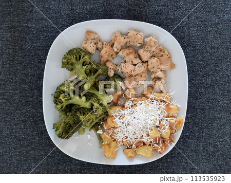 Homemade grilled chicken with french fries, cheese and broccoli, served on a white plate 113535923