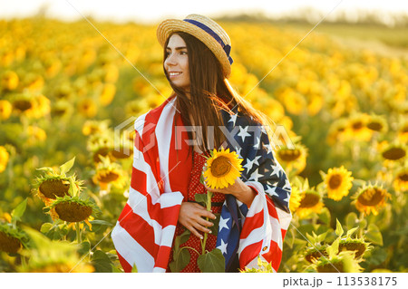 Beautiful girl in hat with the American flag in a sunflower field. 4th of July. Fourth of July. Freedom 113538175