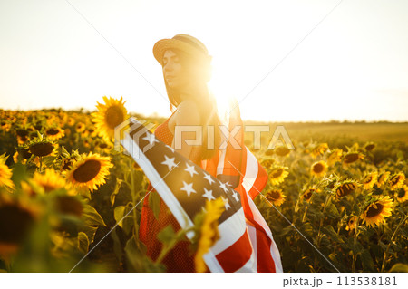 Beautiful girl in hat with the American flag in a sunflower field. 4th of July. Fourth of July. Independence Day. 113538181