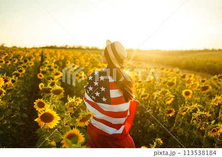 Beautiful girl in hat with the American flag in a sunflower field. 4th of July. Fourth of July. Independence Day. 113538184
