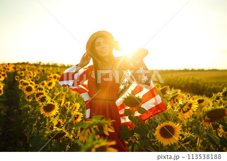 Beautiful girl in hat with the American flag in a sunflower field. 4th of July. Fourth of July. Independence Day. 113538188
