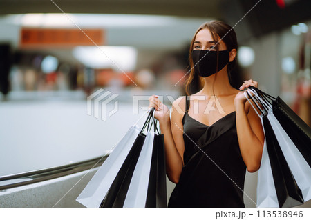 Young woman in protective black medical mask on her face with shopping bags in the mall.Covid-2019. Young woman in protective black medical mask on her face with shopping bags in the mall.Covid-2019. 113538946