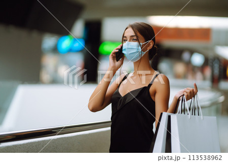 Woman wearing protective medical mask with shopping bags in the mall. Talking on a mobile phone. 113538962
