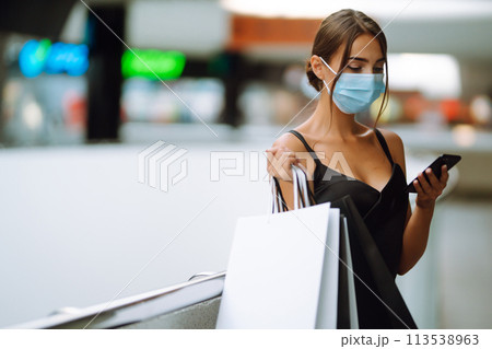 Woman wearing protective medical mask with shopping bags in the mall. Talking on a mobile phone. Woman wearing protective medical mask with shopping bags in the mall. Talking on a mobile phone. 113538963