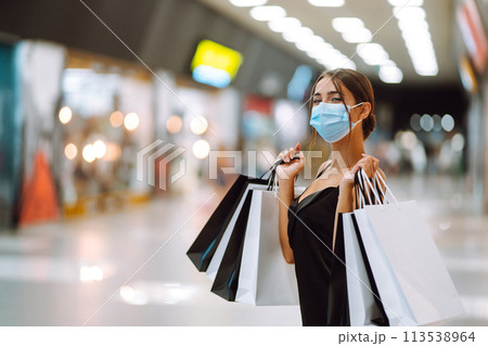 Fashionable woman in protective medical mask with shopping bags walking in the mall. Covid-19. 113538964