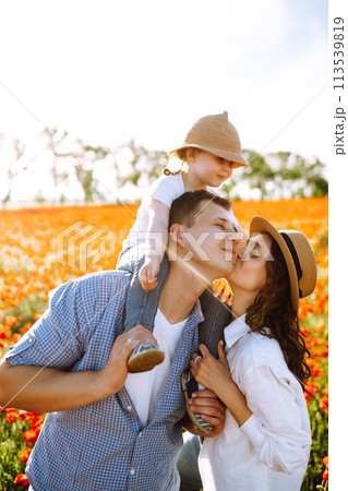 Family with a child walking on a poppy field. Mother, father, little daughter having fun on the poppy field. 113539819