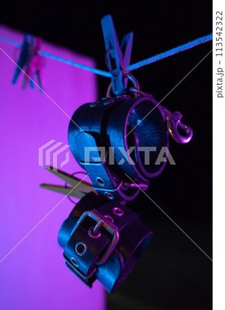 bdsm leather handcuffs hanging on a clothesline in neon light on a black background 113542322