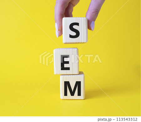 SEM - Search Engine Marketing symbol. Wooden cubes with words SEM. Businessman hand. Beautiful yellow background. Business and SEM concept. Copy space. 113543312