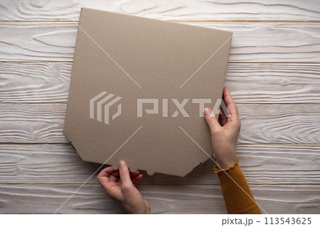 Pizza closed carton box in human caucasian hands on white wooden table flat lay mockup with blank space Pizza closed carton box in human caucasian hands on white wooden table flat lay mockup with blank space 113543625