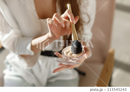 Woman's hands with professional cosmetic tools for make up: brush and powder. Makeup artist in studio. Woman wearing a white costume. Woman's hands with professional cosmetic tools for make up: brush and powder. Makeup artist in studio. Woman wearing a white costume. 113545243