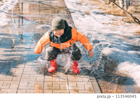 Gleeful Puddles : With every step, the child's red boots send a cascade of droplets into the air, a celebration of melting snow on a sunny day 113546045