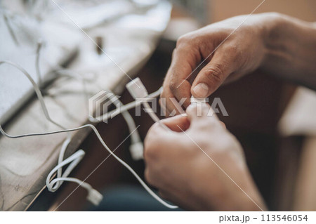 Entangled Solutions - A close-up of hands meticulously selecting the right cable from a tangled assortment, symbolizing the complexity and precision needed in technological troubleshooting 113546054