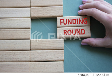 Funding Round symbol. Concept words Funding Round on wooden blocks. Beautiful grey green background. Businessman hand. Business and Funding Round concept. Copy space. 113548156