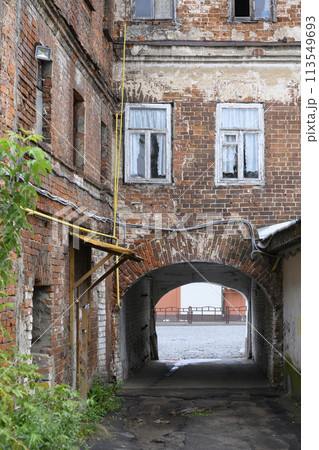 Urban landscape with peeling brick wall of old house with windows, yellow pipes and arched passage 113549693