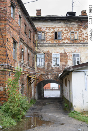 Urban landscape with peeling brick wall of old house with windows, yellow pipes and arched passage 113549695