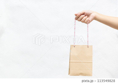 Hand of business woman hold brown paper shopping bag on white concrete background Hand of business woman hold brown paper shopping bag on white concrete background 113549828