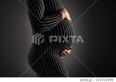 Elegant Pregnant Woman Embracing Her Belly in Striped Dress 113551099