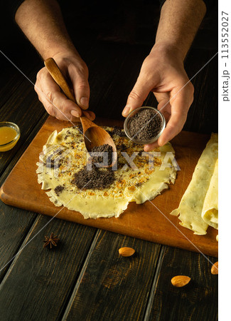 The cook adds poppy seeds to the pancakes on the kitchen table with a spoon. Low key concept for preparing the Ukrainian national dish Nalisniki The cook adds poppy seeds to the pancakes on the kitchen table with a spoon. Low key concept for preparing the Ukrainian national dish Nalisniki 113552027