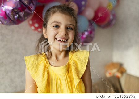Laughing real girl 7 years old in yellow dress against backdrop of festive balloons in holiday at home 113552875